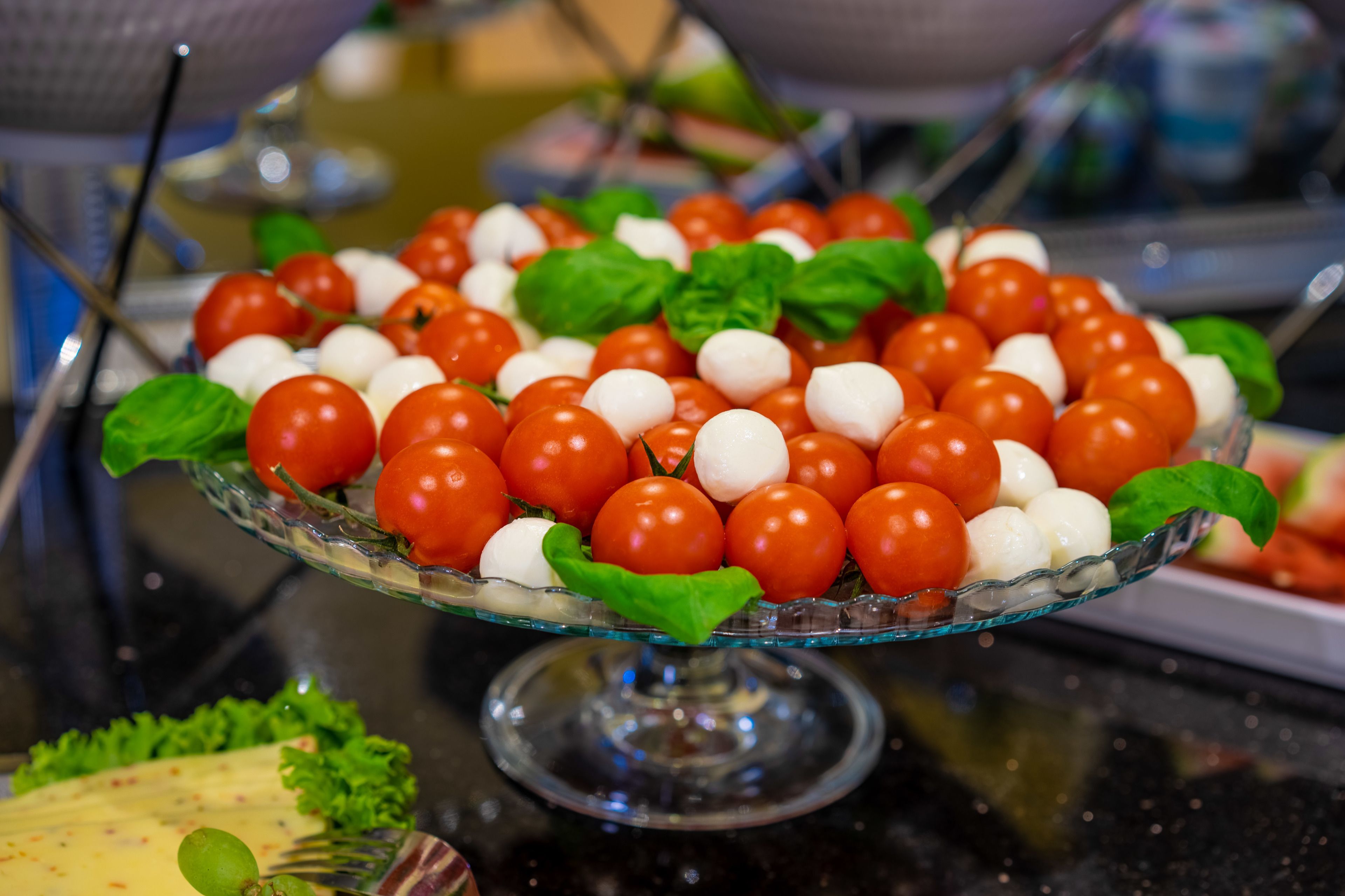 A glass serving dish with cherry tomatoes and mozzarella balls, garnished with basil leaves.