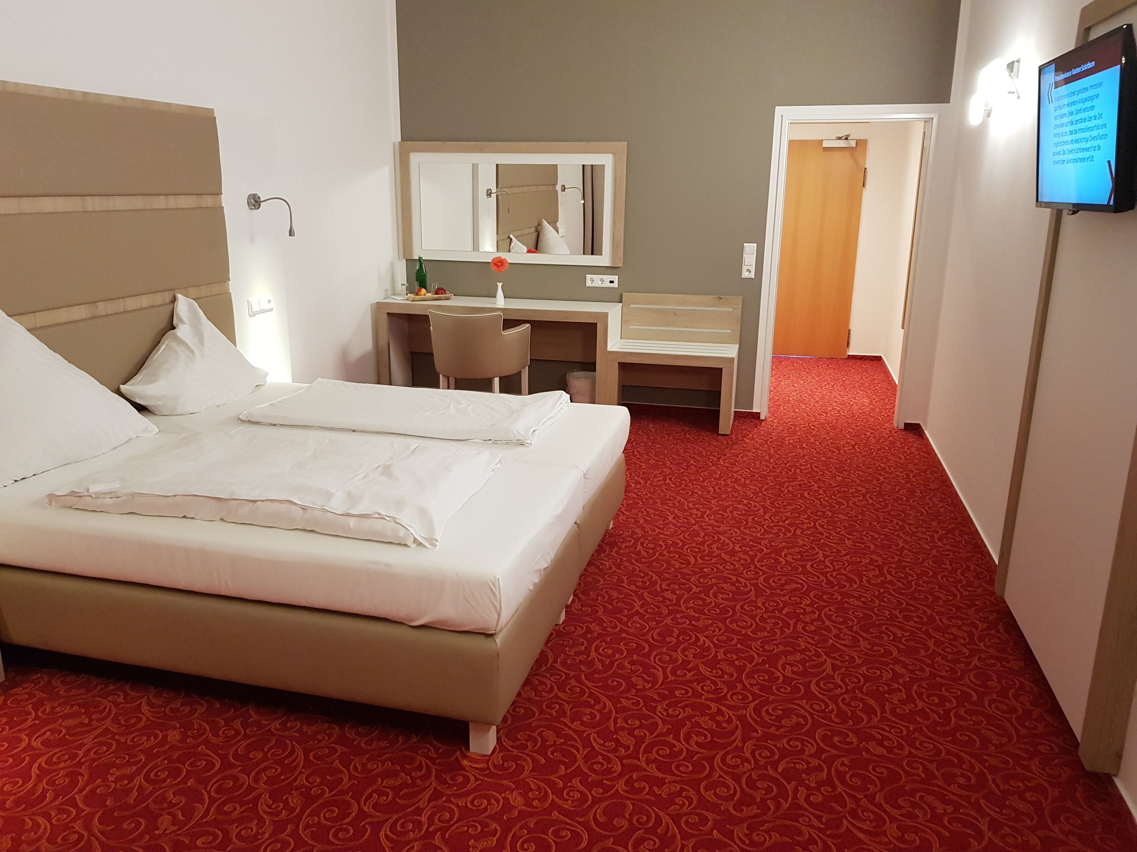 Una habitación de hotel con una cama, un escritorio, una silla, un espejo y un televisor.