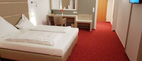 Una habitación de hotel con una cama, un escritorio, una silla, un espejo y un televisor.