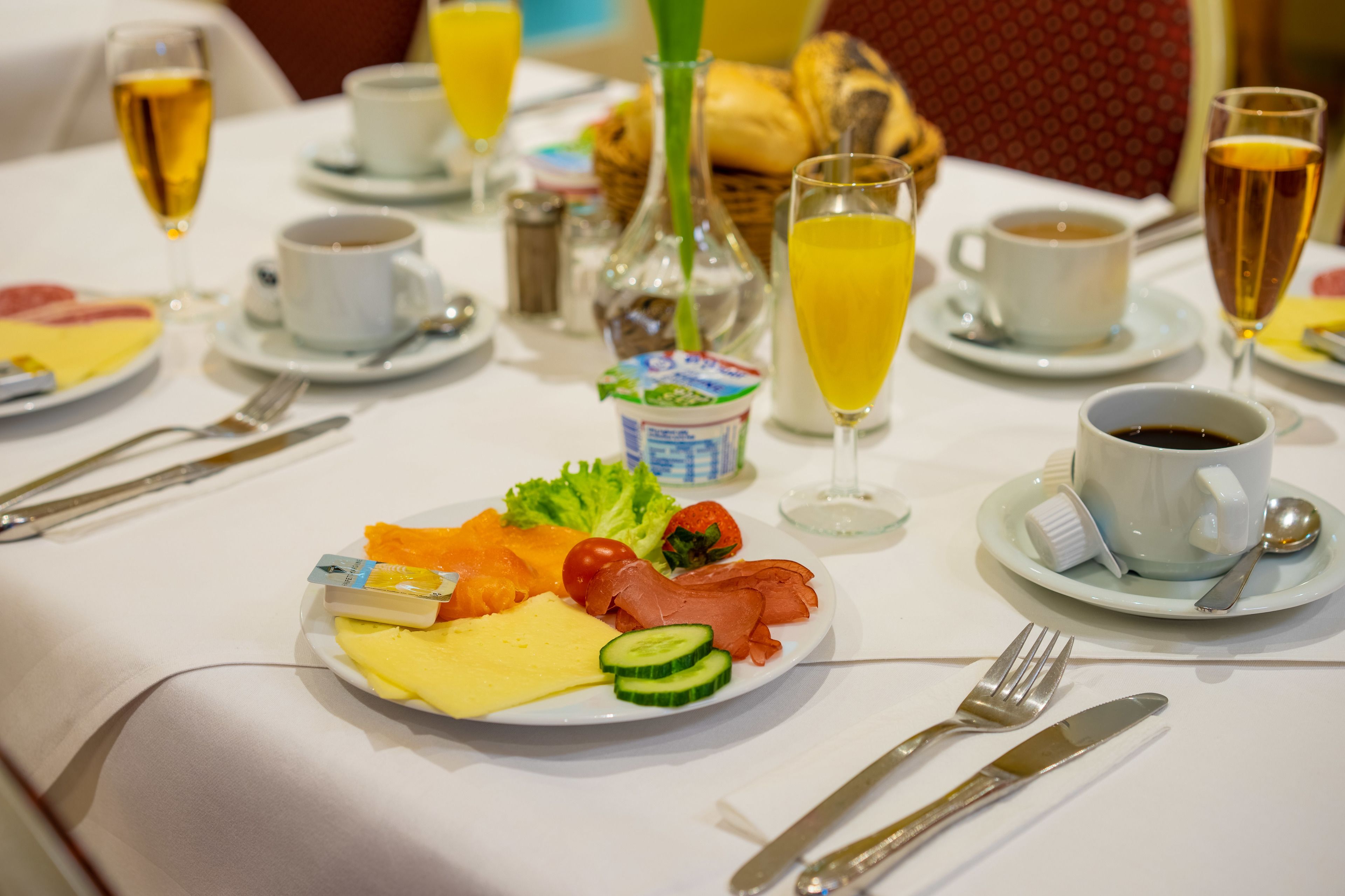 Un desayuno con un plato de huevos, jamón, queso y verduras, acompañado de café, jugo y una botella de leche.