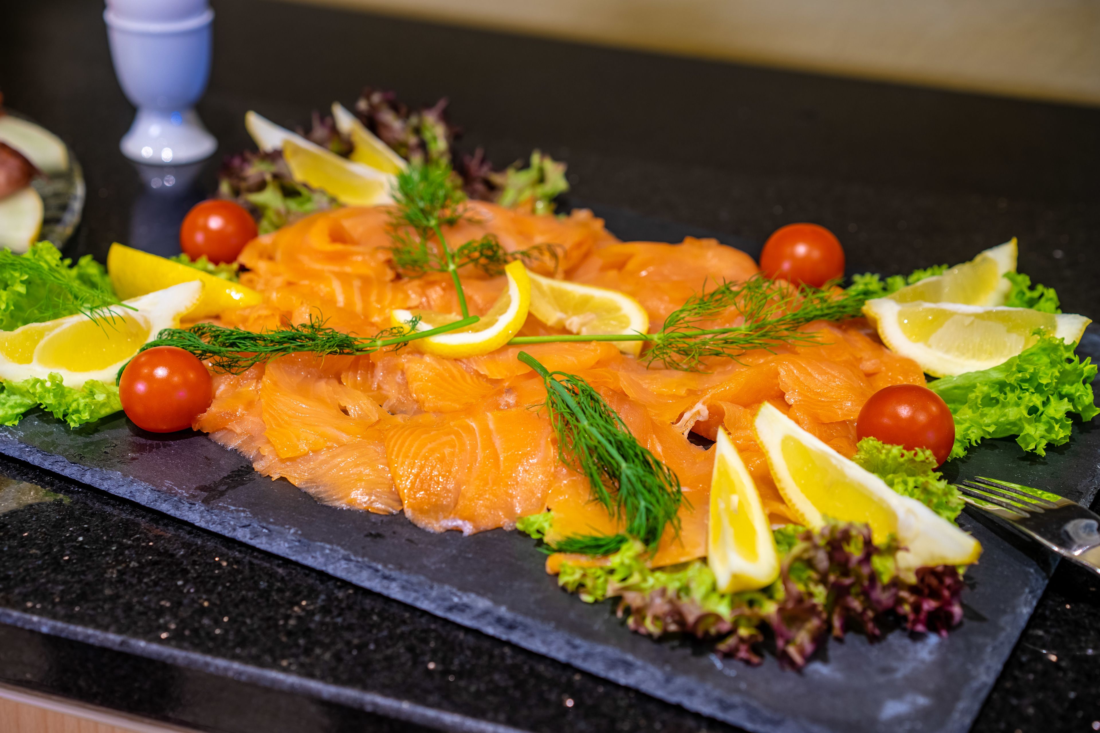 A platter of smoked salmon garnished with dill, lemon slices, and cherry tomatoes on a slate board.