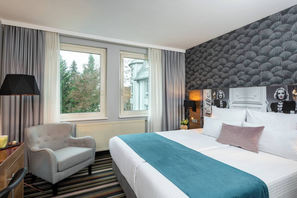 A hotel room with a bed, a chair, a desk, and a window with curtains.