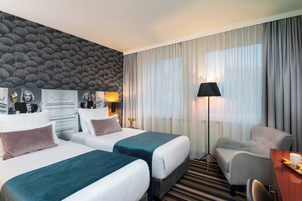 A hotel room with two beds, a sofa, a desk, and a lamp.