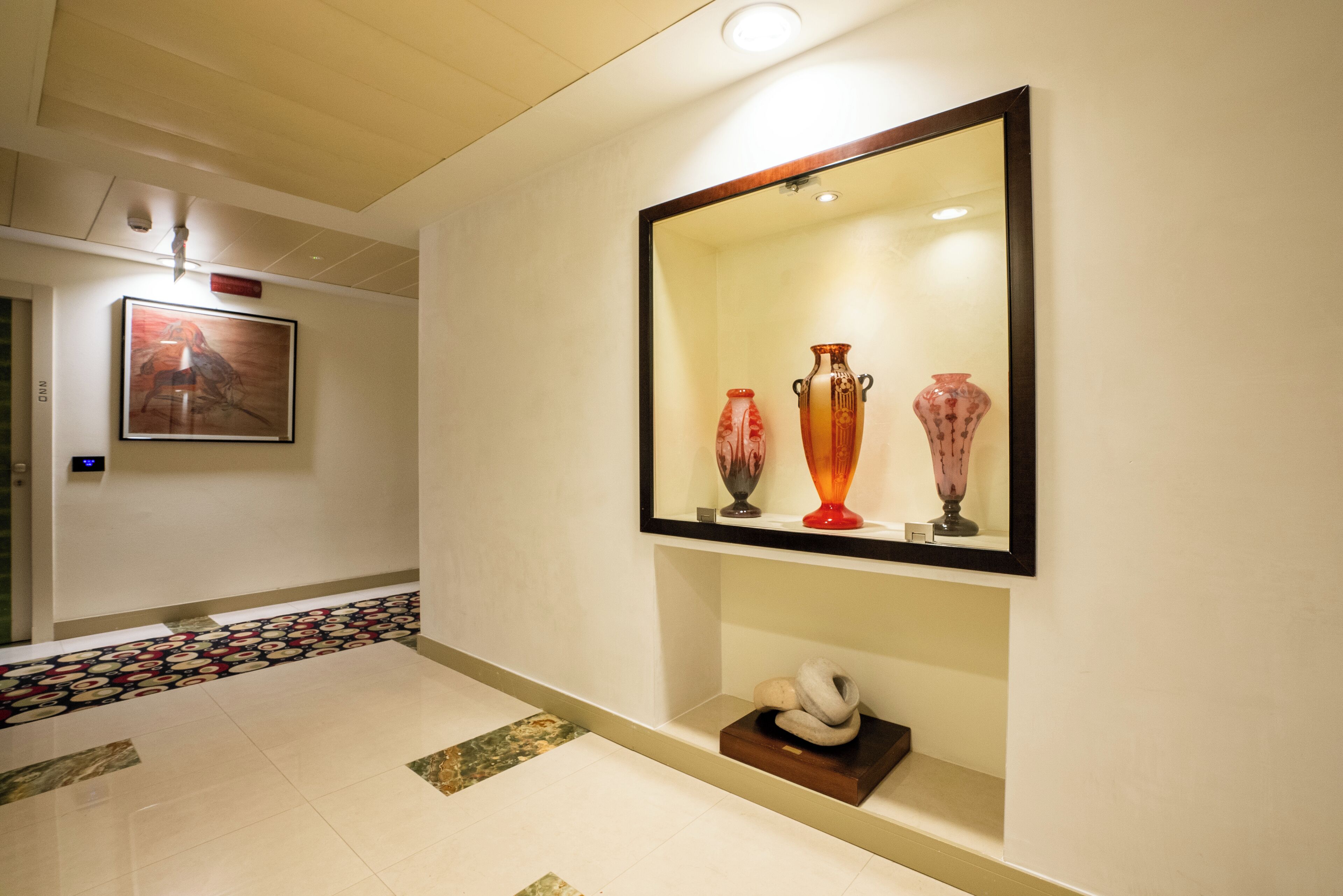 A hallway with a tiled floor, a framed mirror, and three vases on a shelf.