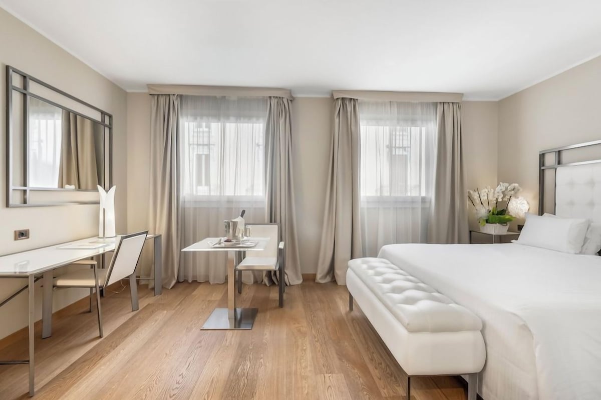 Habitación de hotel con cama, escritorio, silla, mesita pequeña y banco.