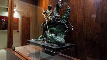 Uma estátua de bronze de uma figura montada a cavalo, exposta sobre um pedestal de madeira numa vitrine de vidro.