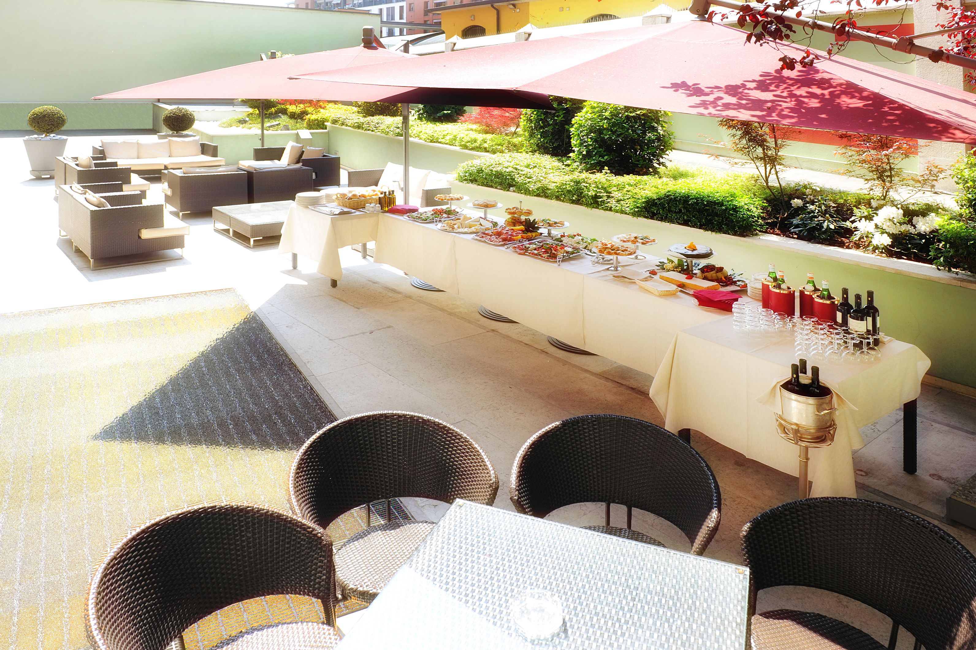 Un área de comedor al aire libre con mobiliario de mimbre, una mesa de buffet y un paraguas rojo.