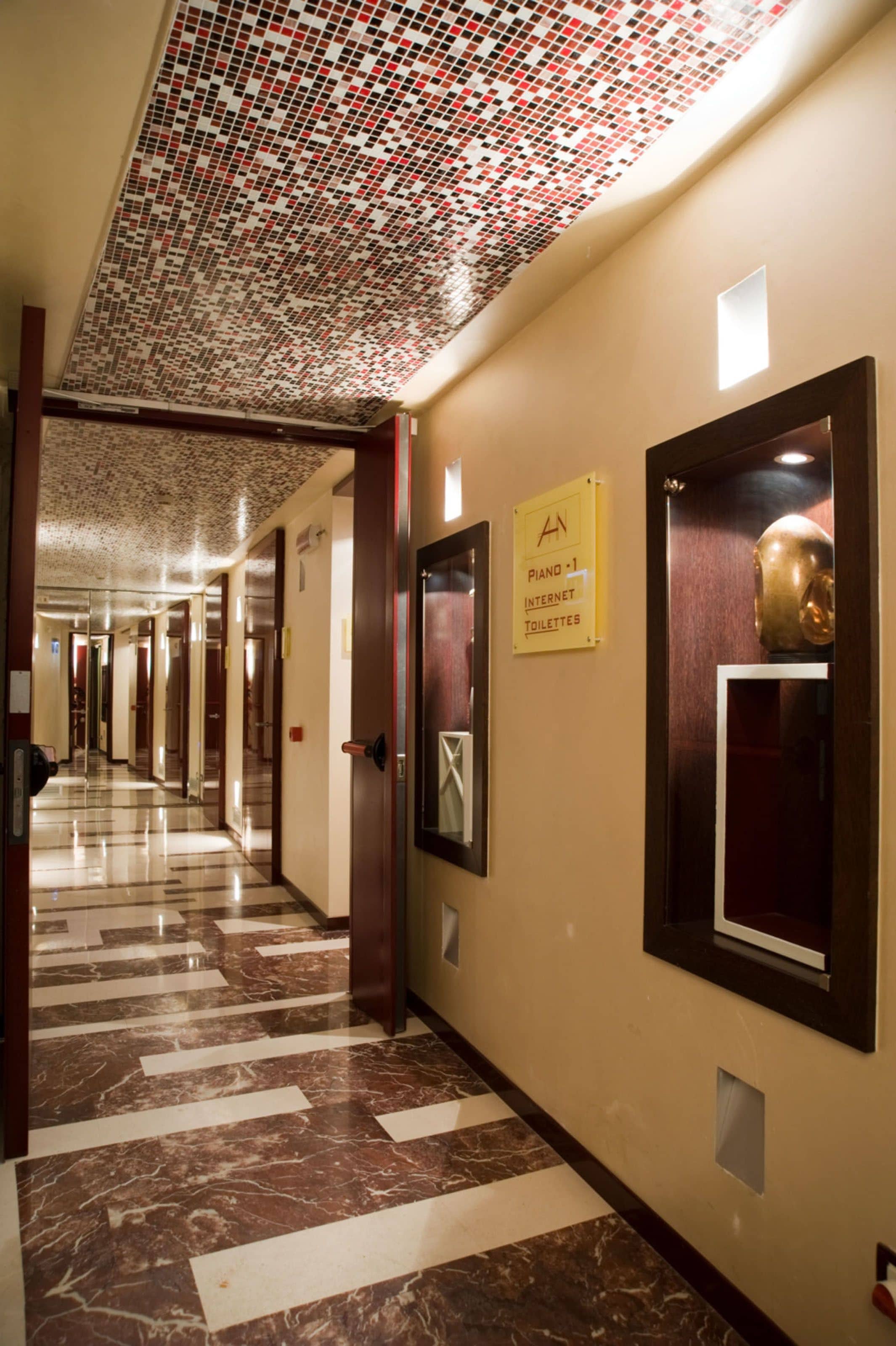 Un pasillo de hotel con techo estampado, suelo de mármol y carteles que indican servicios como piano, internet y baños.