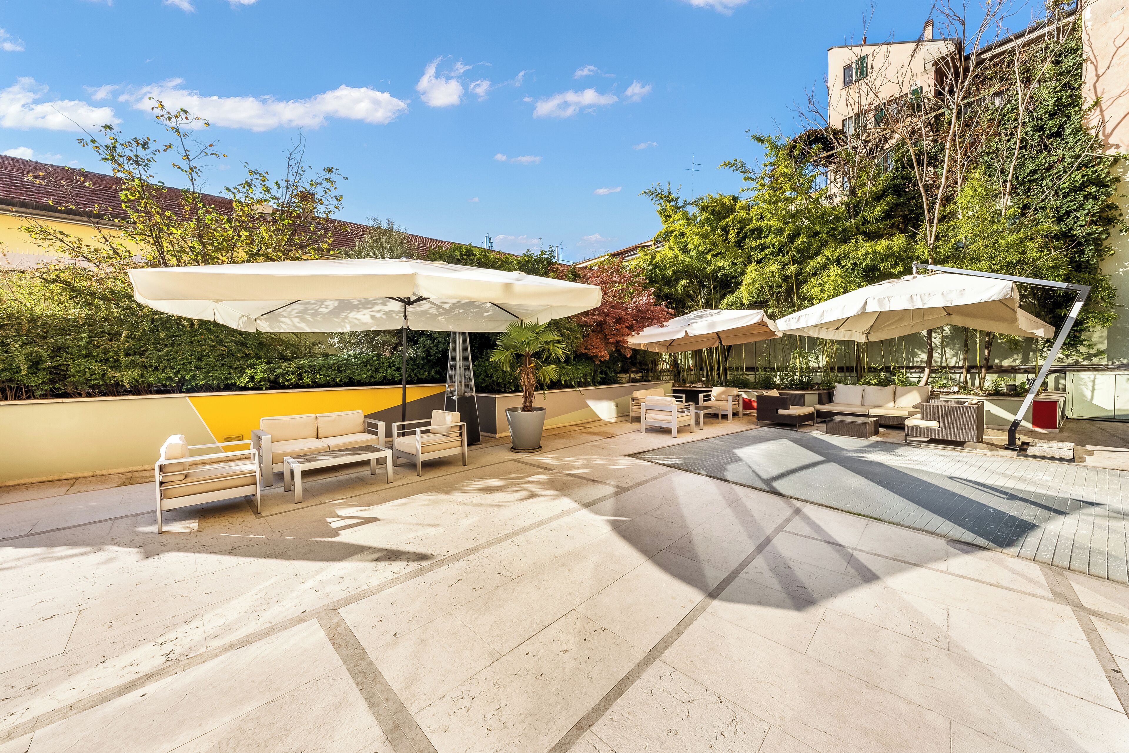 Ein Außenbereich mit Terrasse und verschiedenen Sitzgelegenheiten, darunter Sofas und Stühle, unter großen Sonnenschirmen.