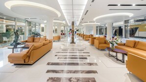 Un vestíbulo amplio con mobiliario moderno, una escalera central y un muro de cristal que ofrece vistas del interior.