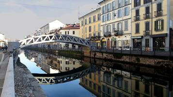 A canal with a bridge, buildings with balconies, and a reflection in the water.