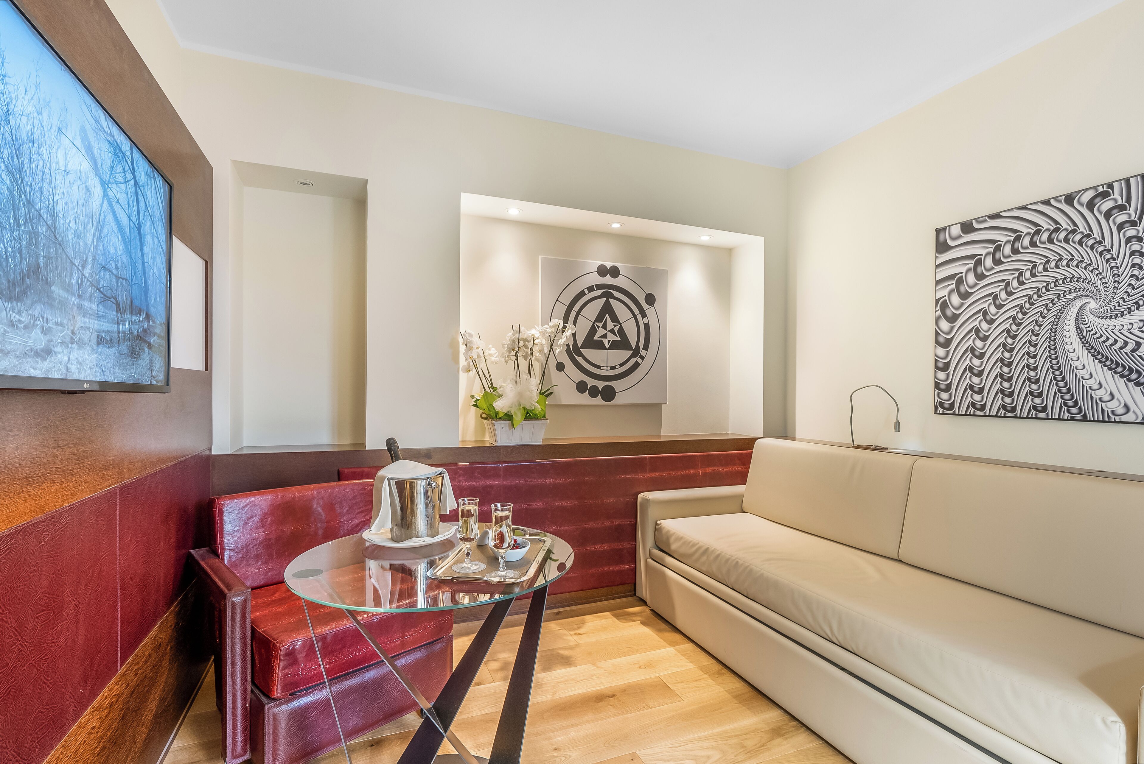A modern living room with a glass coffee table, red leather seating, a beige sofa, and artwork on the walls.