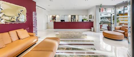 A modern hotel lobby with a reception desk, seating area, and a view of the outside.