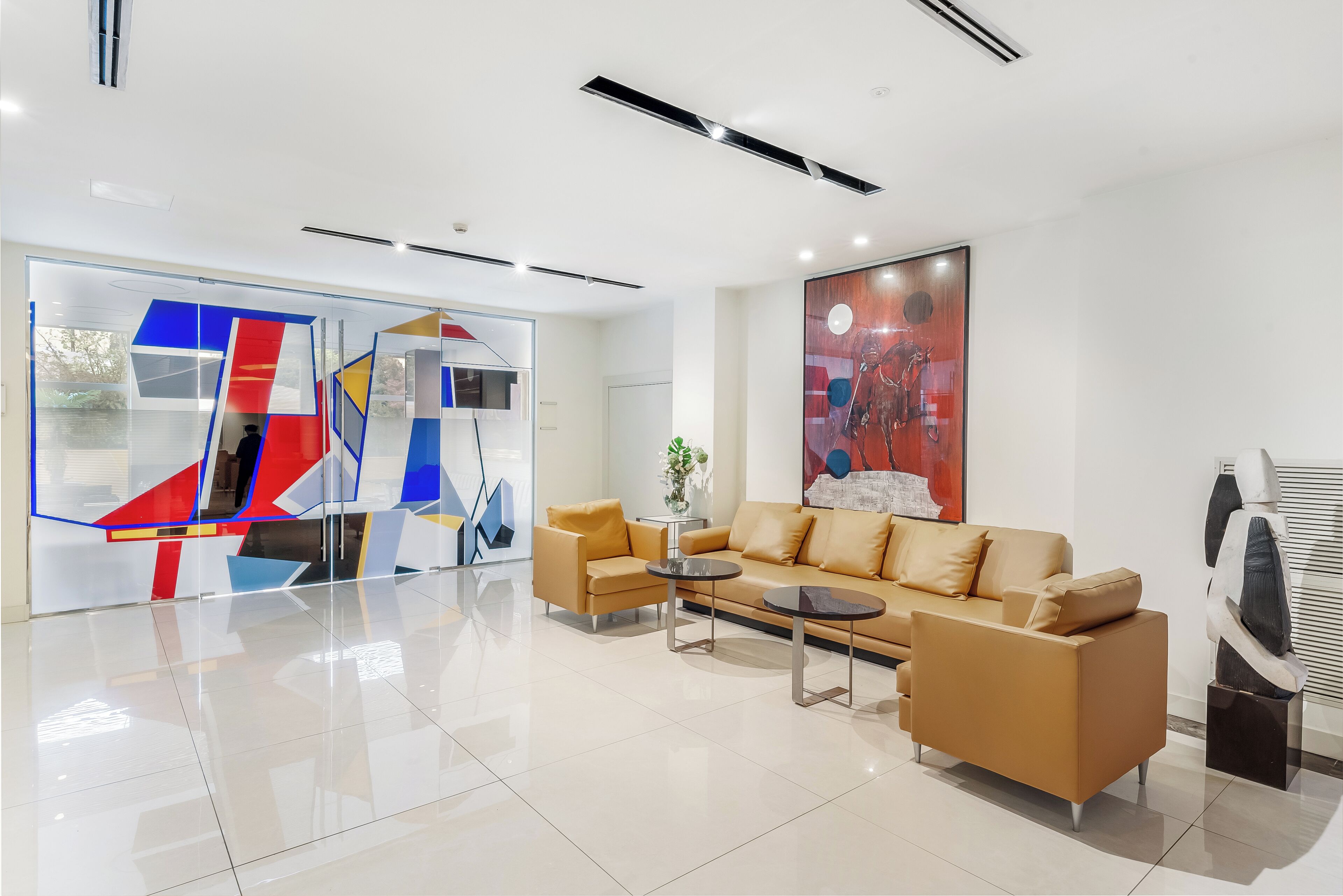 A modern lobby with a beige sofa, two coffee tables, and a large abstract painting.