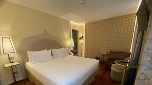 Una habitación de hotel con una cama grande, lámparas de noche, una silla y una mesita.
