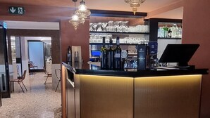 Un vestíbulo con piso de terrazo, una recepción con computadora y una zona de bar con estantes llenos de vasos y botellas.