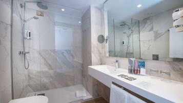 Un baño moderno con ducha de vidrio, lavabo blanco y un espejo grande.