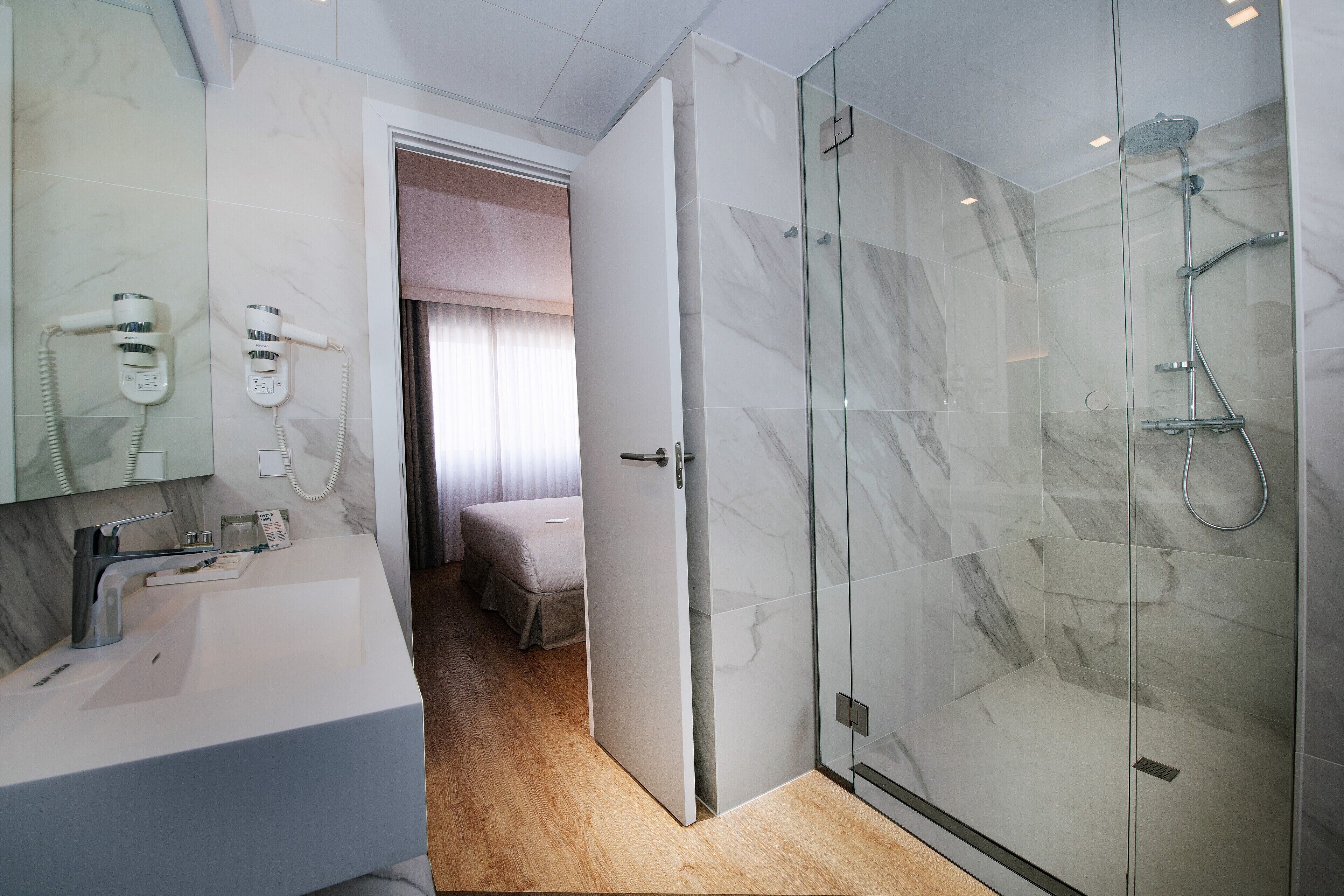 A modern bathroom with a glass-enclosed shower, a white sink, and a hairdryer mounted on the wall.