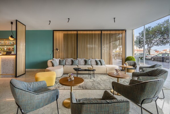 A modern lounge area with a sofa, armchairs, and a coffee table. A bar with bottles is visible on the left. - Occidental Vigo (Vigo)