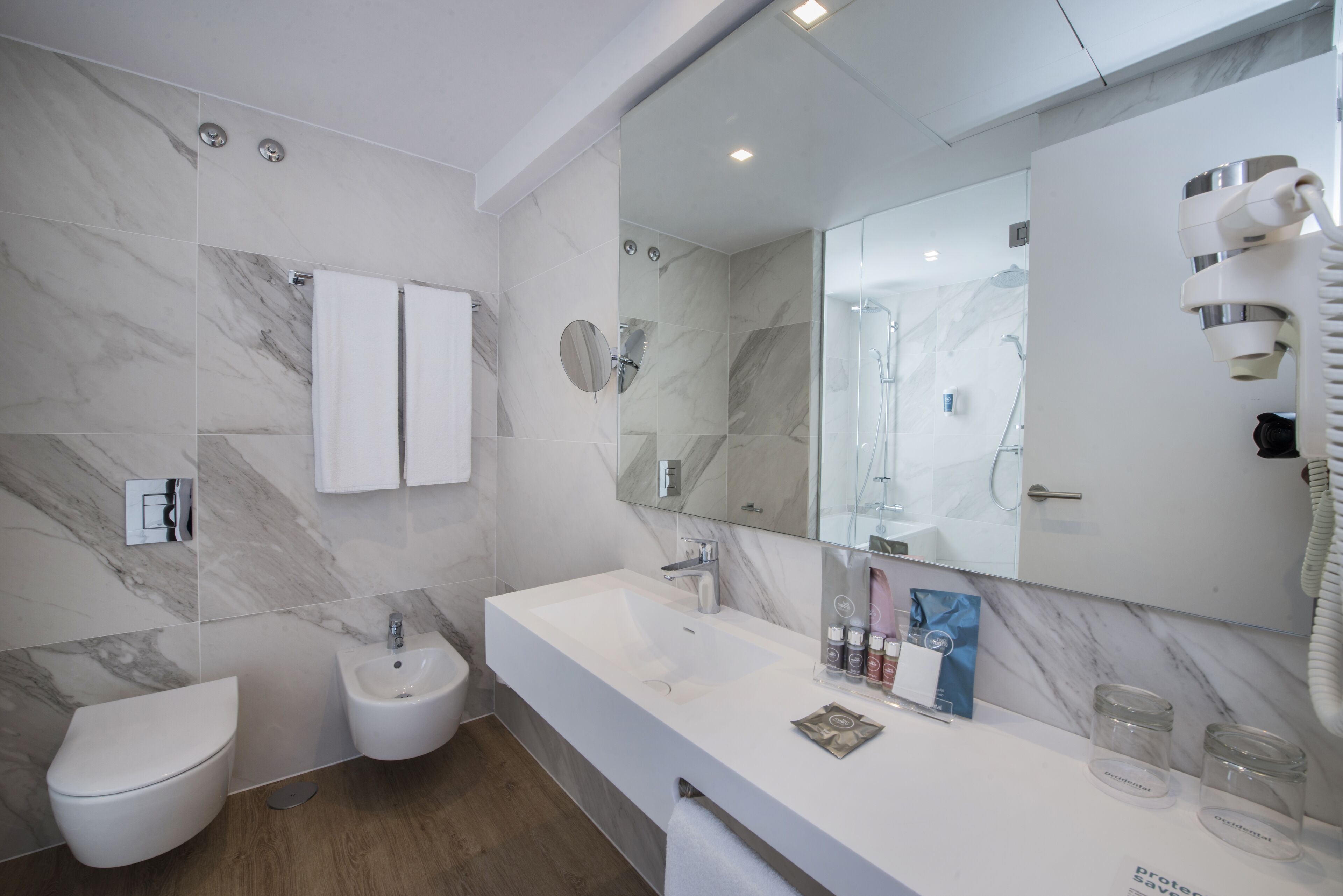 Ein modernes Badezimmer mit einem großen Spiegel, einem weißen Waschbecken, einem Bidet und Marmorwänden.