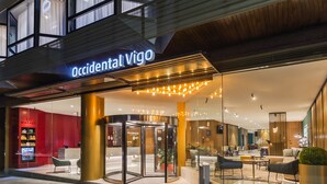 A hotel entrance with a revolving door, a reception desk, and a seating area with modern furniture. - Occidental Vigo (Vigo)