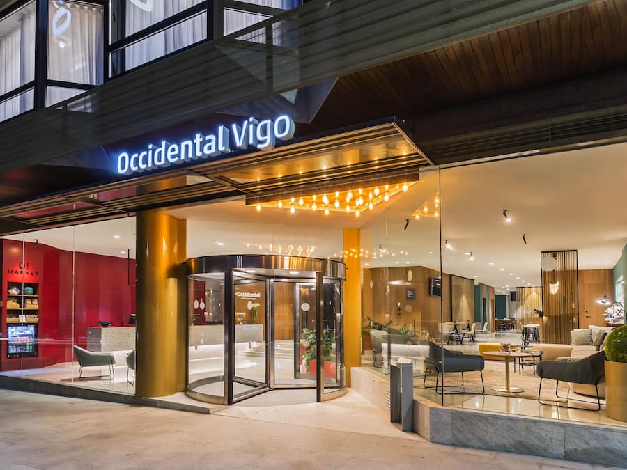 L’entrée d’un hôtel, avec une porte tournante, un comptoir d’accueil et un espace détente doté de mobilier moderne.