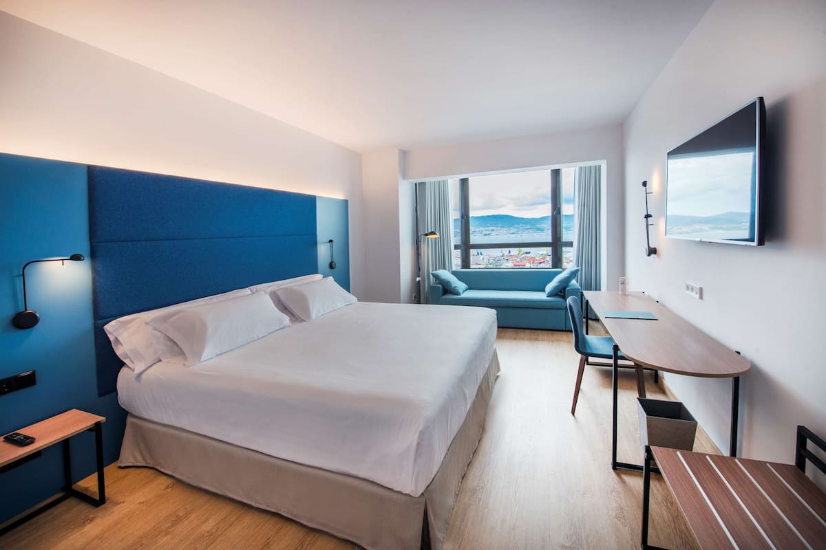 Ett modernt hotellrum med en stor säng, ett skrivbord och utsikt över stadsbilden.