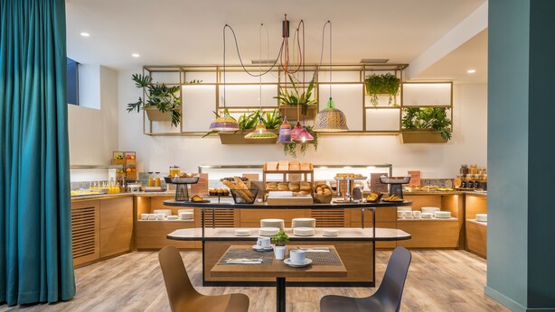 A modern breakfast bar with a wooden table, two chairs, and a variety of breakfast items. - Occidental Vigo (Vigo)