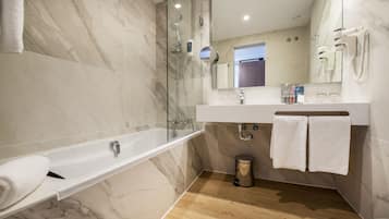 Un baño moderno con ducha de vidrio, una bañera blanca, tocador con espejo y piso de madera.