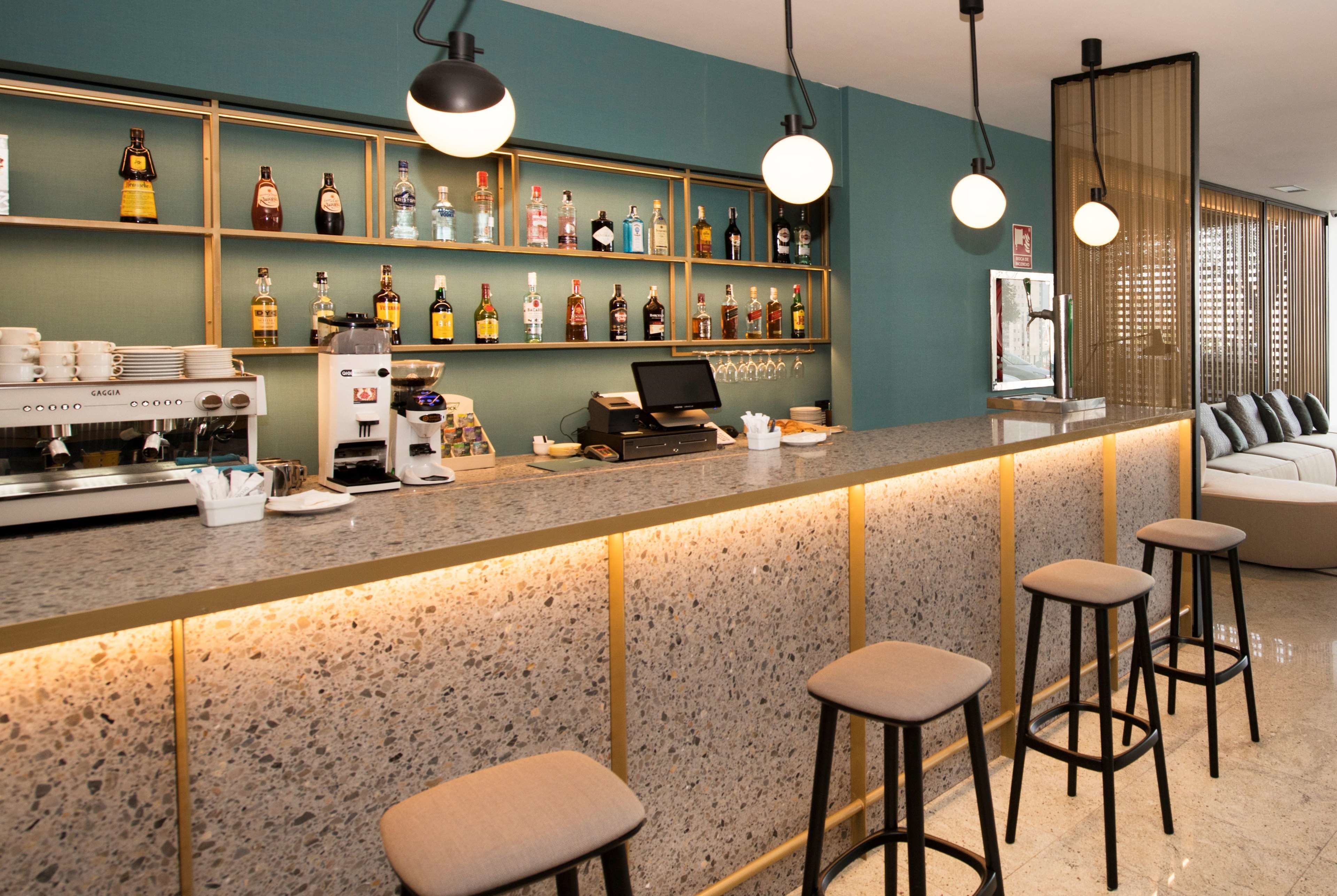 A bar area with a granite countertop, bar stools, a coffee machine, and shelves with various bottles.