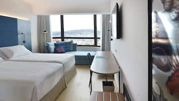A hotel room with two beds, a desk, a chair, a view of the city, and a TV on the wall.