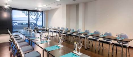 Un salón de conferencias con mesas largas, sillas y botellas de agua.