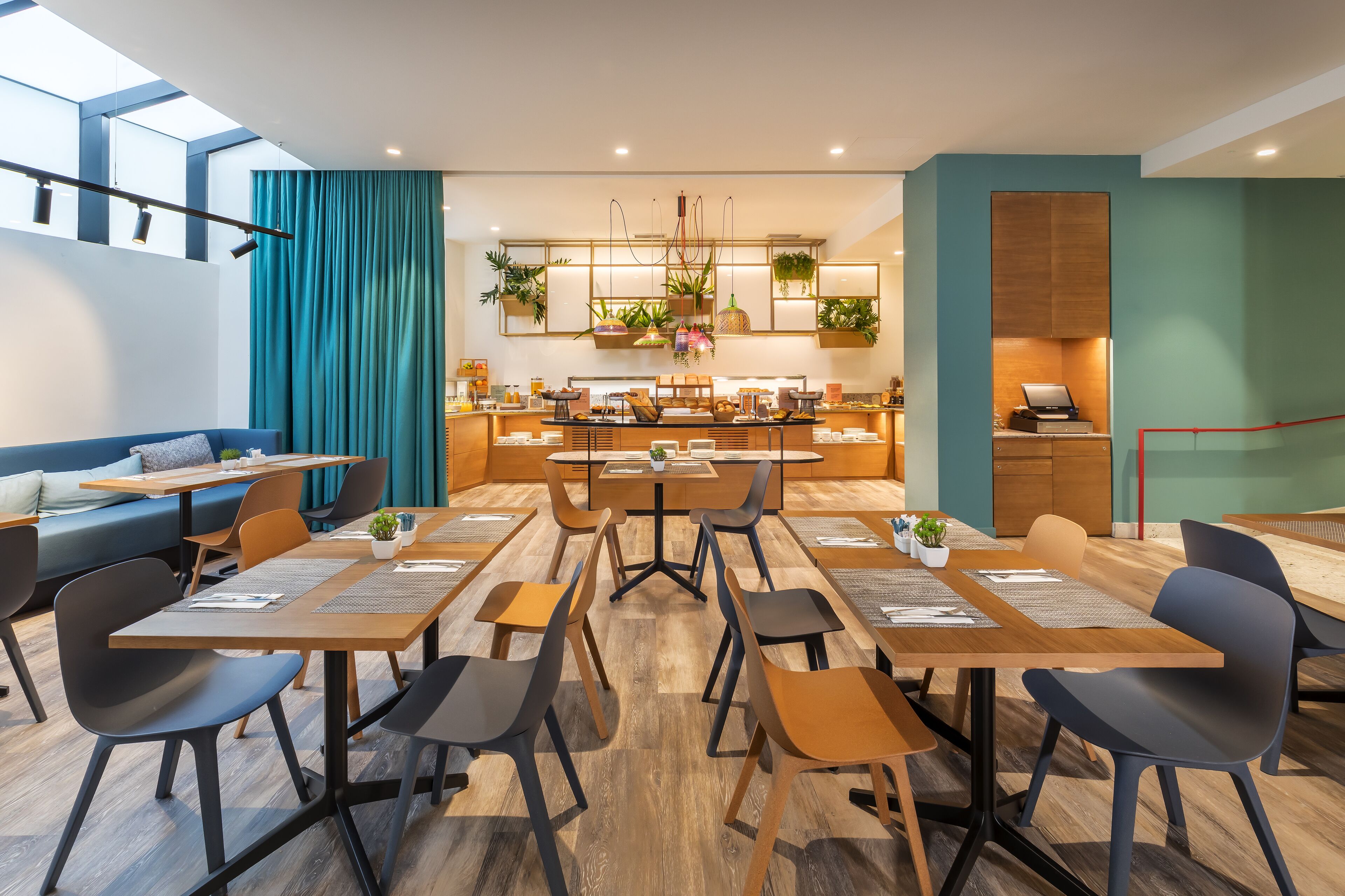 A modern dining area with wooden tables and chairs, a blue sofa, and a kitchen in the background.