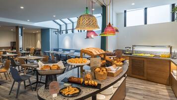 Zona de dinar d'un hotel modern amb un sistema de menjar a gran bufet, incloent pa, pastissos i diverses opcions per esmorzar.