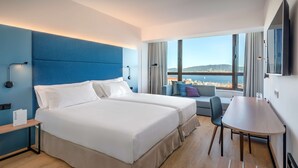 A modern hotel room with two beds, a dining table, and a large window offering a city view. - Occidental Vigo (Vigo)