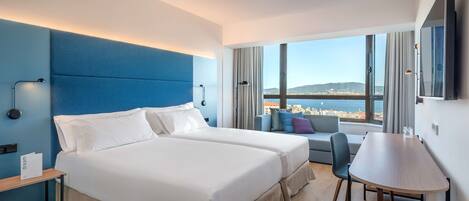 Una habitación de hotel moderna con dos camas, una mesa de comedor y un ventanal con vistas a la ciudad.