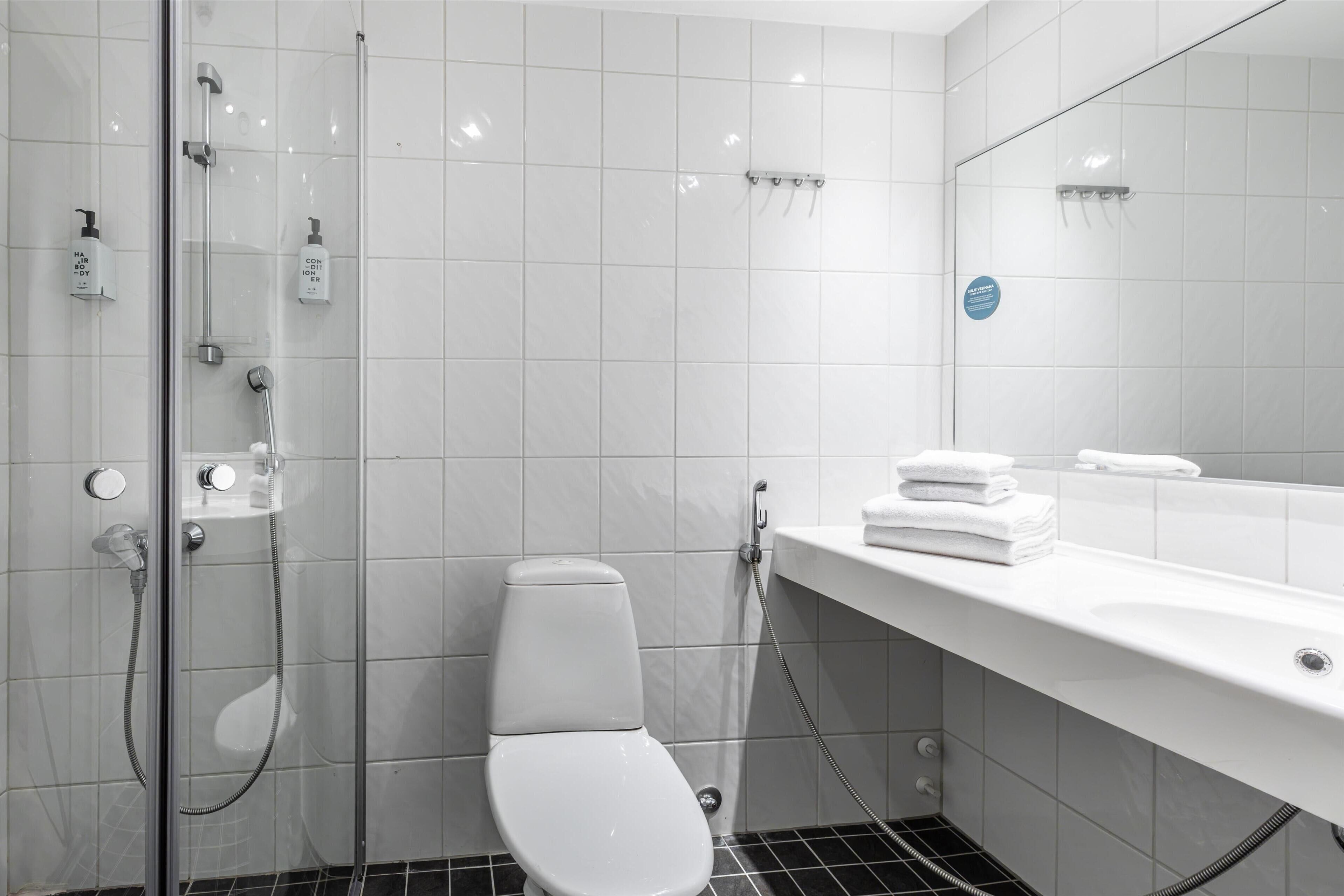 Un baño moderno con ducha de vidrio, inodoro blanco y bañera blanca con una pila de toallas.