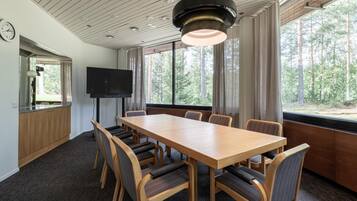 Un salón de conferencias con una larga mesa, sillas, una televisión y ventanas amplias con vistas a un bosque.