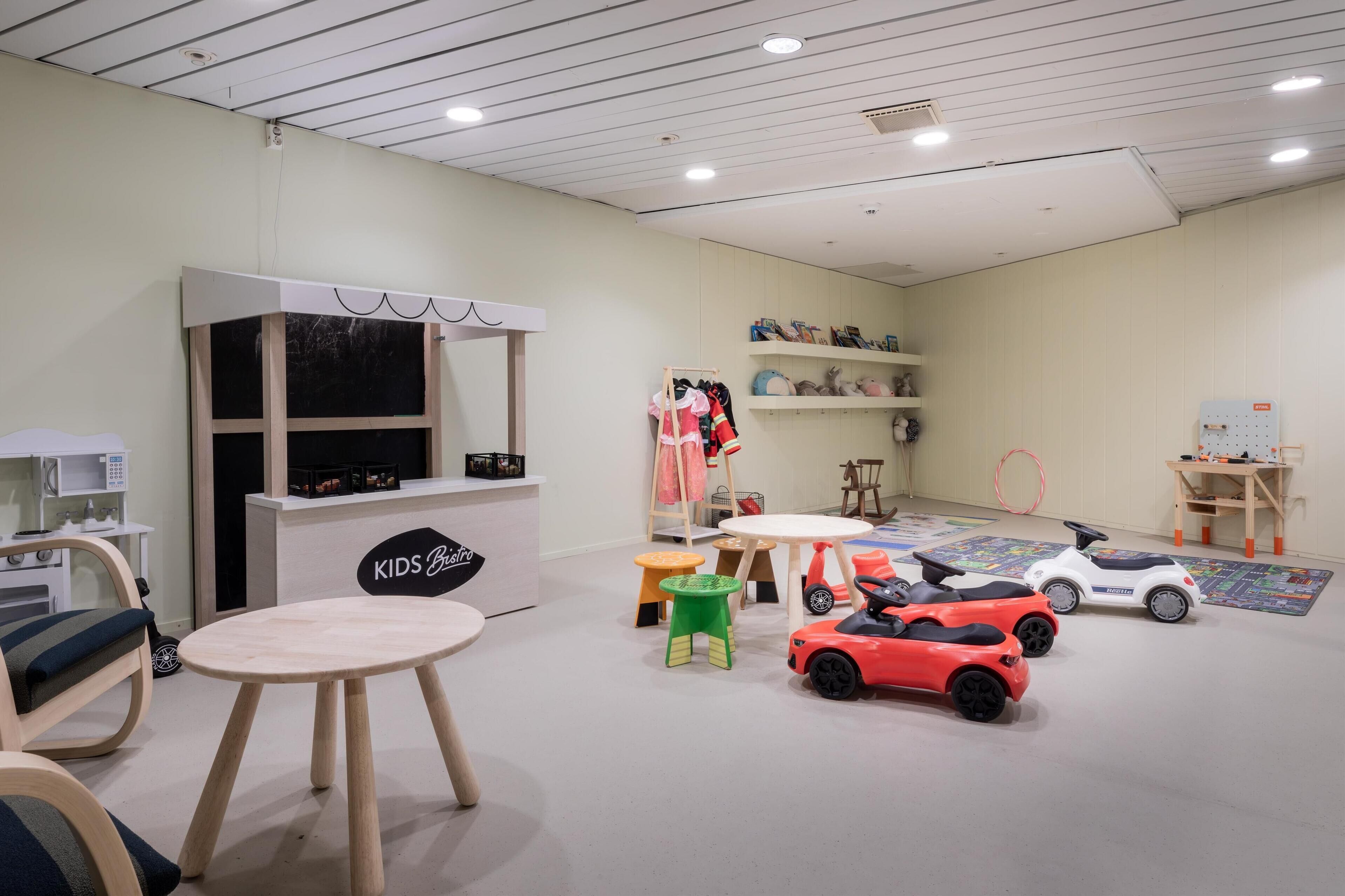 A children's play area with a kitchenette, a table, chairs, and various toys including toy cars.