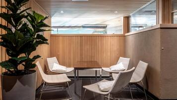 A modern indoor seating area with a wooden wall, a large potted plant, and a view of an outdoor swimming pool.
