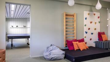 Una stanza con tavolo da ping pong, parete da arrampicata, pouf e divano con cuscini.