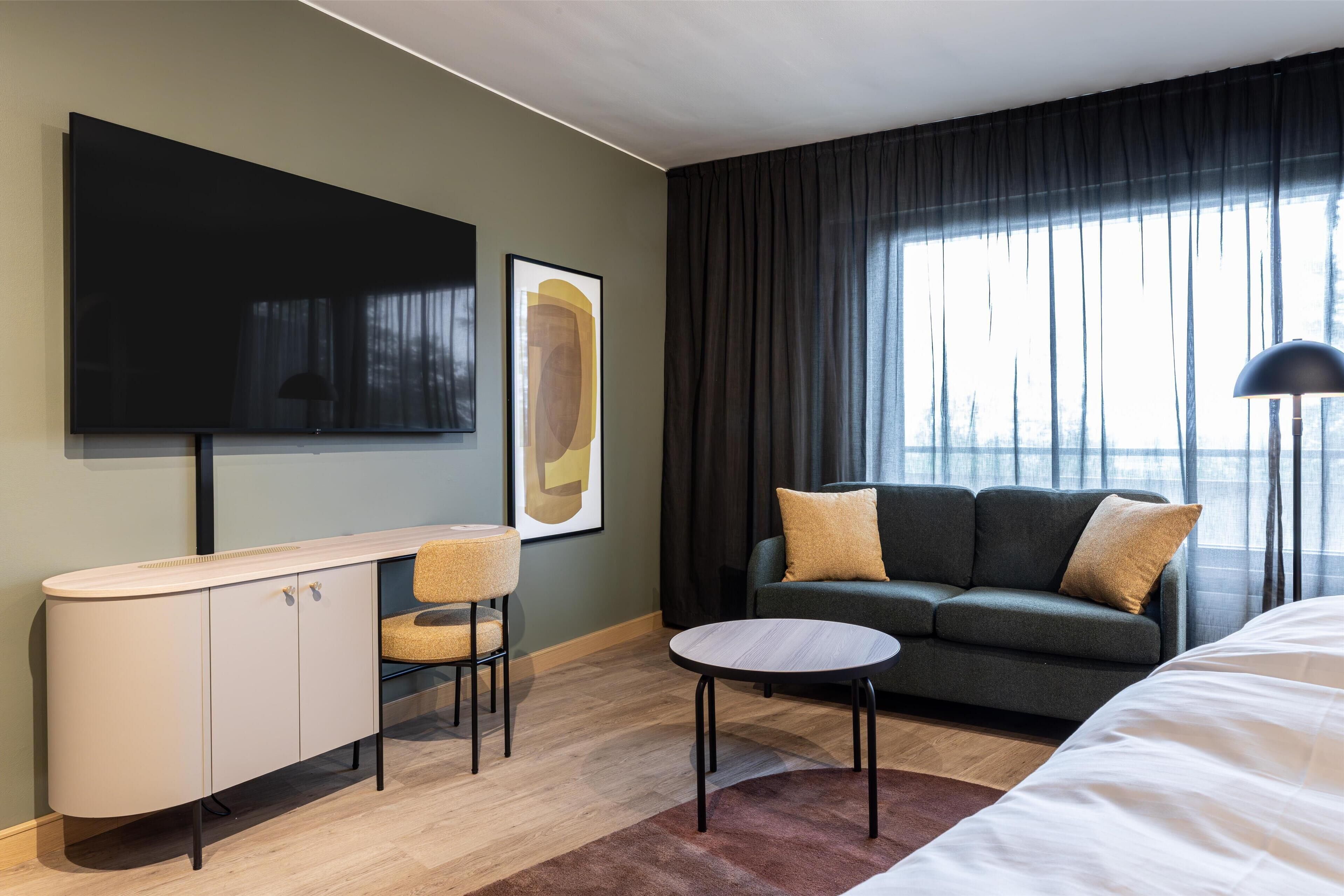 A modern hotel room with a flat-screen TV, a sofa, a small round table, and a bed.