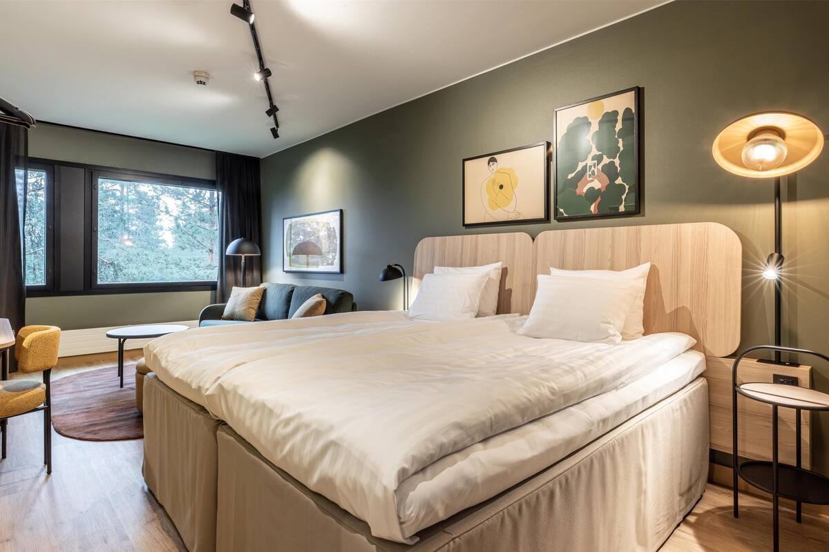 Une chambre d’hôtel moderne, dotée d’un grand lit, d’un bureau, d’une chaise et d’une fenêtre donnant sur la verdure.