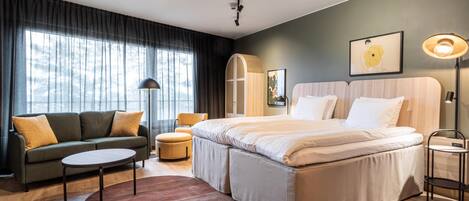 A modern hotel room with a large bed, a sofa, a small table, and a chair.