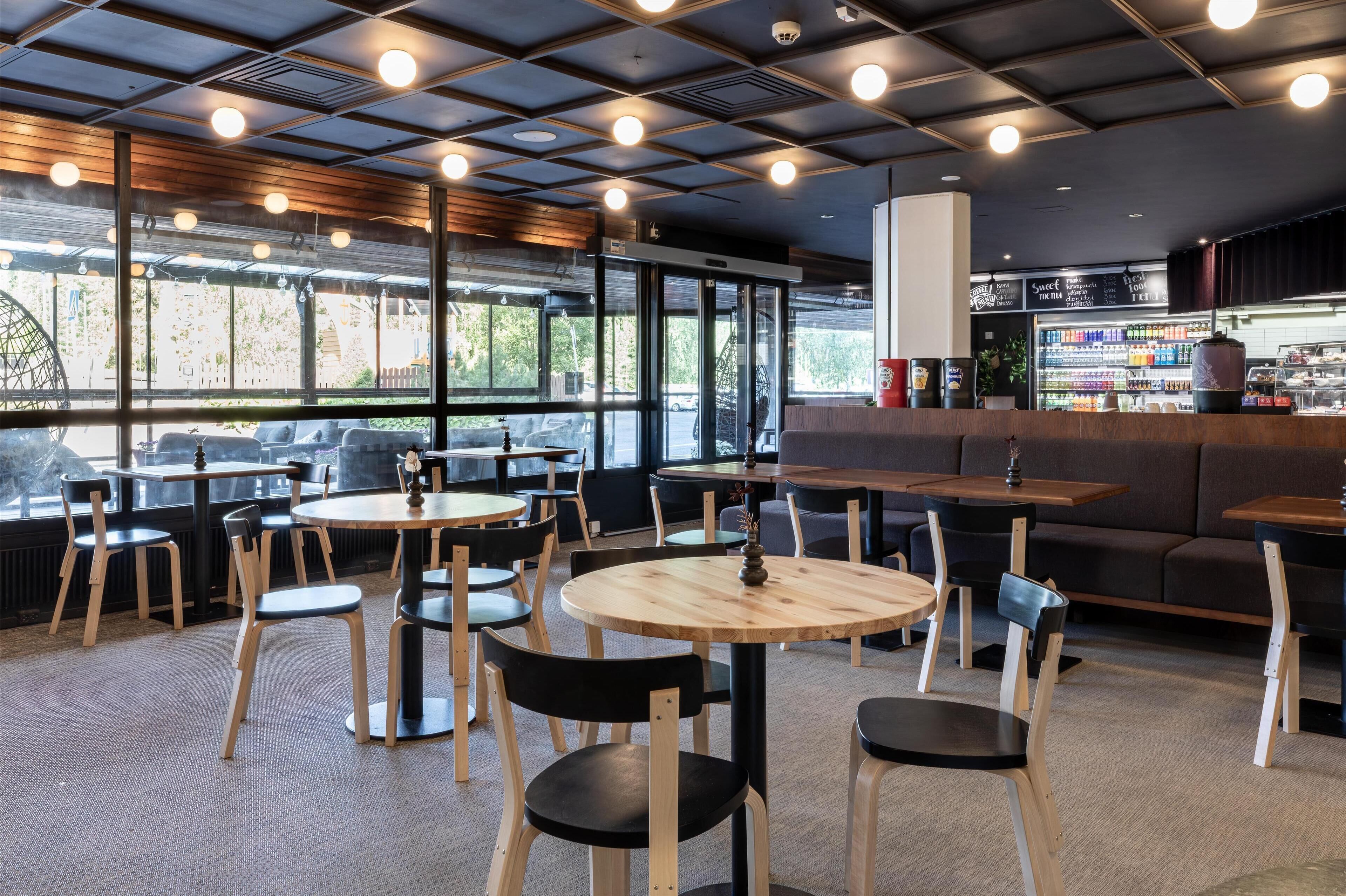 Un café moderno con mesas redondas y sillas negras, ventanas amplias con vistas y una zona de bar con menú.