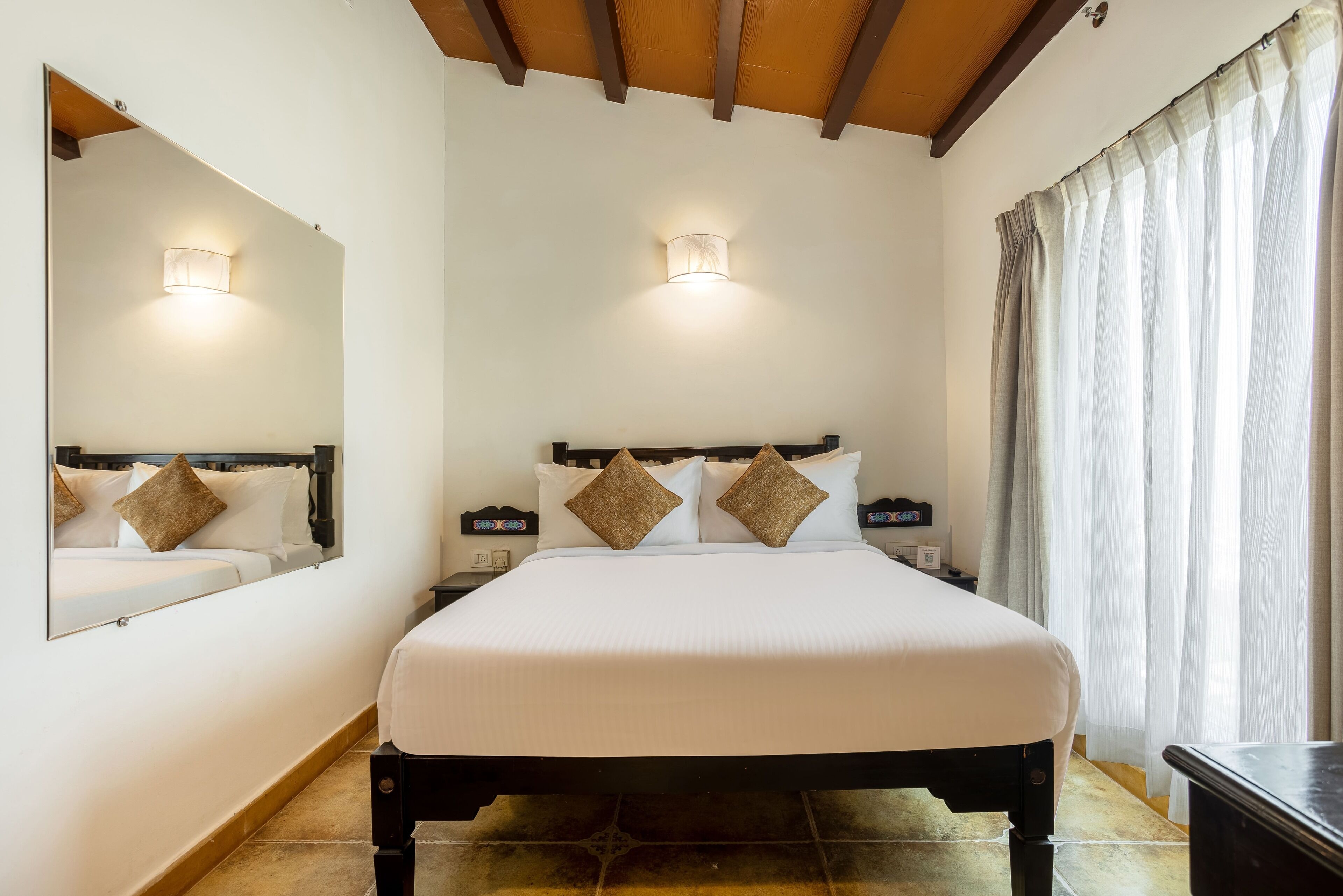 A neatly made bed with a headboard, two bedside tables with lamps, a large mirror, and a window with curtains.
