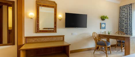 A hotel room with a wooden bench, a TV mounted on the wall, and two wicker chairs.