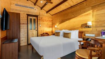 A wooden cabin room with a bed, a desk, a chair, a TV, and a lamp.