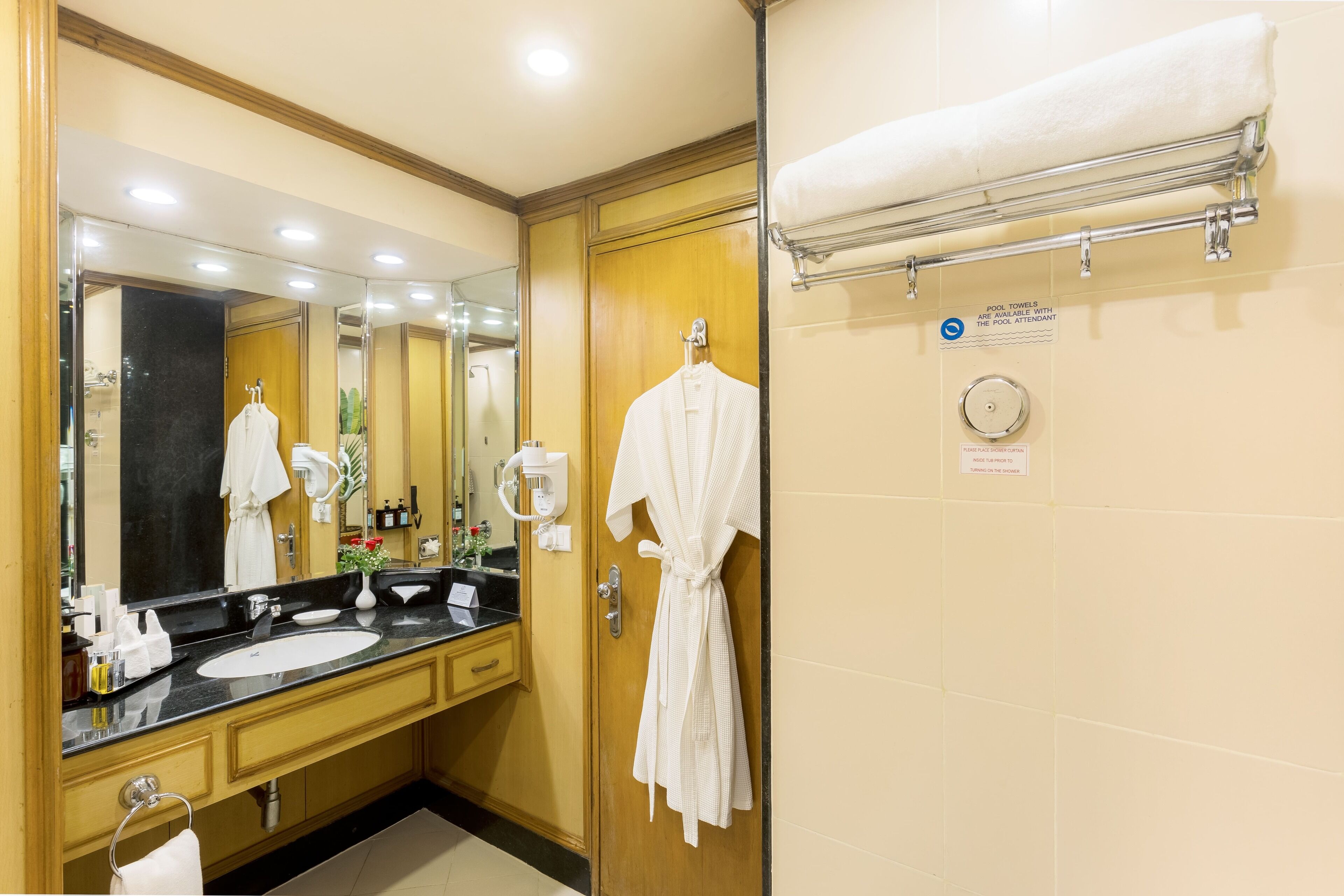 Um banheiro de hotel com um espelho grande, duas pias, um porta-robes e um porta-toalhas.