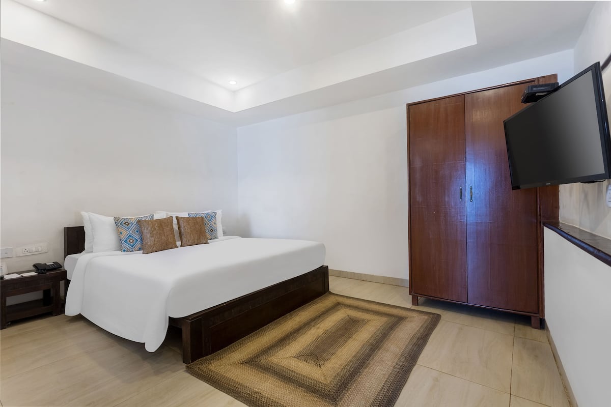 A bedroom with a bed, bedside table, nightstand, wardrobe, and a TV mounted on the wall.